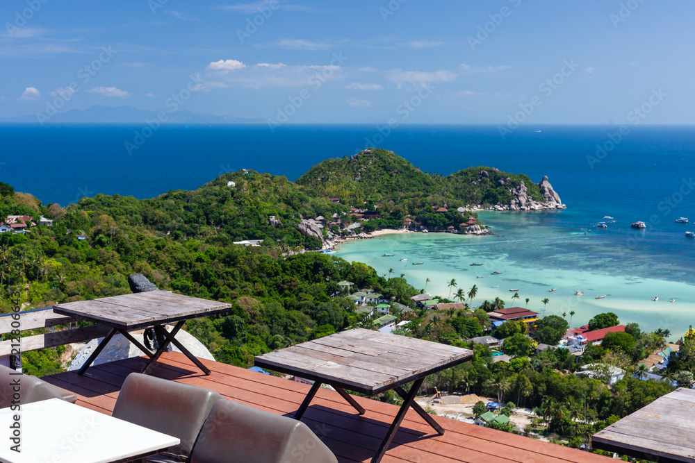 Fototapeta premium Wooden tables and chairs on an outdoor terrace overlooking a scenic tropical island view in Koh Tao, Thailand.