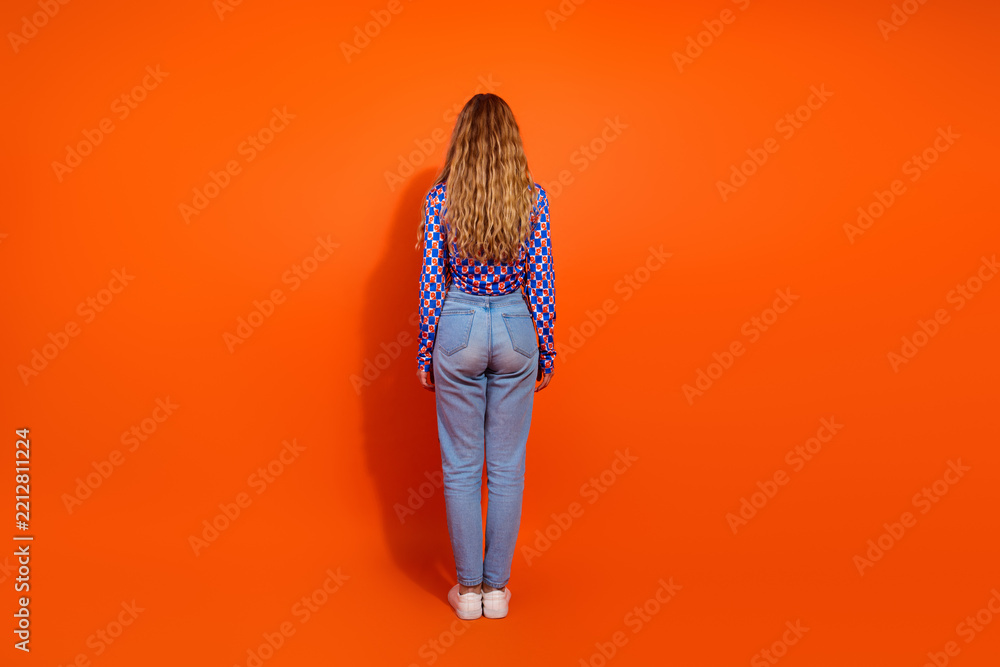 Fototapeta premium Attractive young woman in checkered outfit standing confidently against vibrant orange backdrop showcasing casual style