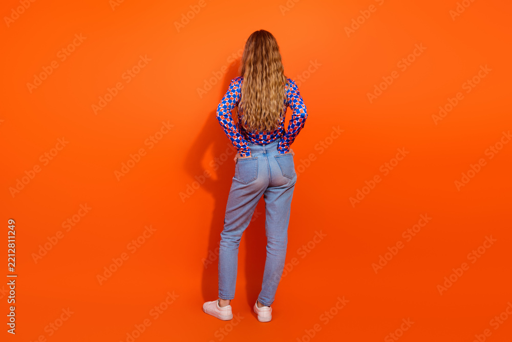 Fototapeta premium Fashionable young woman standing confidently against orange background in stylish casual attire with a unique top