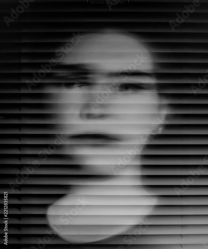 Ghostly abstract portrait of a young woman in closeup with motion blur and venetian blind effect in monochrome black and white