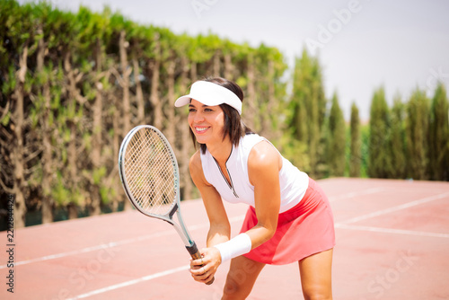 Young woman smiling, holding tennis racket, ready to play on an outdoor court