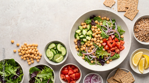 Fresh chickpea salad bowl with diced tomatoes, cucumbers, red onion, greens, whole grain crackers and lemon.