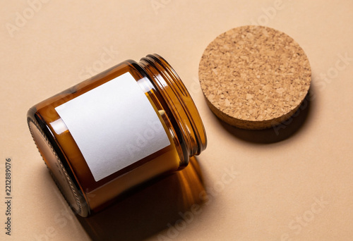 Amber glass jar with white blank label lying on side with cork lid on beige surface