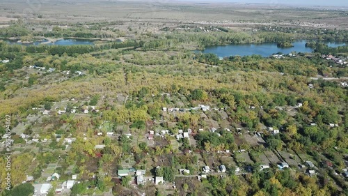 Scenic aerial view of autumn village and lake surrounded by yellow trees on sunny day