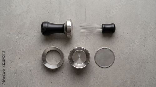  Premium collection of professional barista tools featuring black espresso tamper, wire distribution tool, dosing funnel, and stainless steel filter basket arranged neatly on a textured grey backgroun