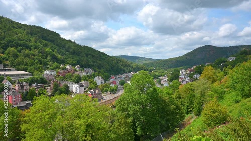 Panoramic view of a charming town nestled in a lush green valley surrounded by forested hills