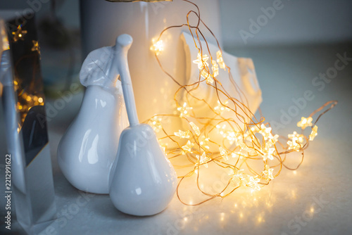 Close-up of white ceramic pear-shaped ornaments beside glowing string of warm star-shaped LED lights on reflective surface.