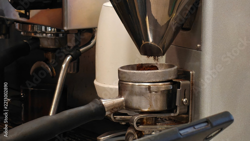 Coffee grinder dispensing fresh ground coffee into a portafilter at a cafe espresso machine
