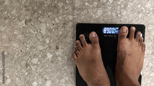 Person stepping on a digital weighing scale showing body weight to monitor fitness and overweight status