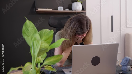 Woman removes her glasses, rubs her face and covers it with both hands while sitting in front of laptop. Concept of work stress and mental exhaustion