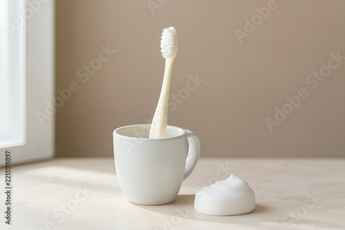 Toothbrush in a ceramic cup with toothpaste on a pale stone counter