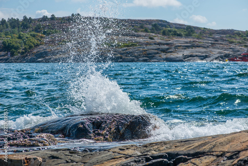 Powerful sea wave splashing dramatically against rocky Swedish shoreline.
