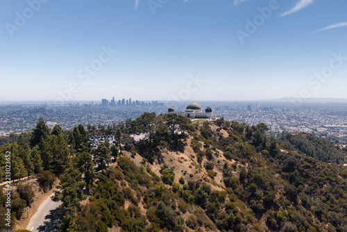 Aerial shot of Griffith Observatory atop Mount Hollywood overlooking the Los Angeles basin with downtown skyscrapers visible under a clear daylight sky, California.