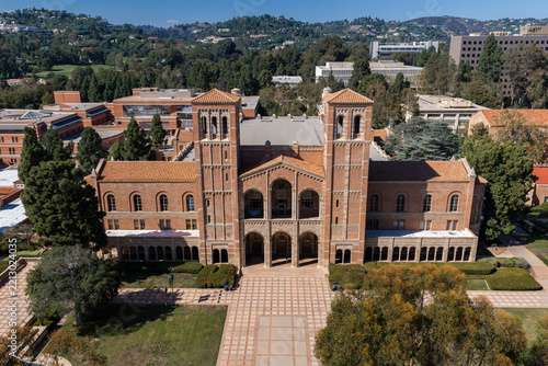 Aerial view of the historic brick facade of Royce Hall on the UCLA university campus in Los Angeles, California, with courtyards and surrounding trees under bright sunlight.