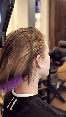 Professional female stylist using hair dryer and purple brush to dry wet hair of a woman client after coloring. Beauty salon workflow, hair care routine process of a local small business