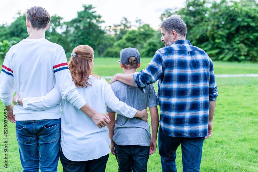 Naklejka premium Back view of a multiracial family of four walking together in a green park