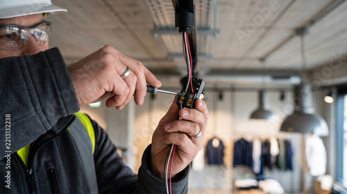 Electrician using a screwdriver to repair electrical wiring in a commercial retail store interior