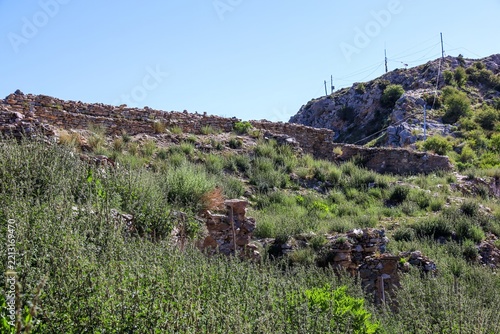 Ruins of former halls destroyed during the Cultural Revolution on the hilltop of Ganden Monastery in Dagze, Tibet, with crumbling stone walls and green hillside vegetation.