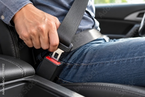 A close-up of a person in a car wearing jeans, fastening their black seatbelt for road safety.