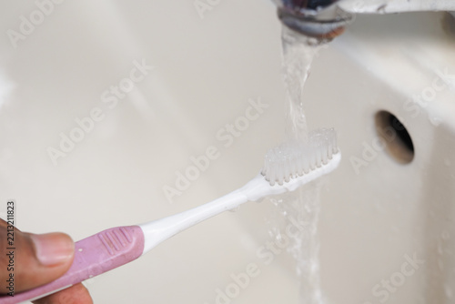 Person brushes teeth with toothbrush under running water in bathroom