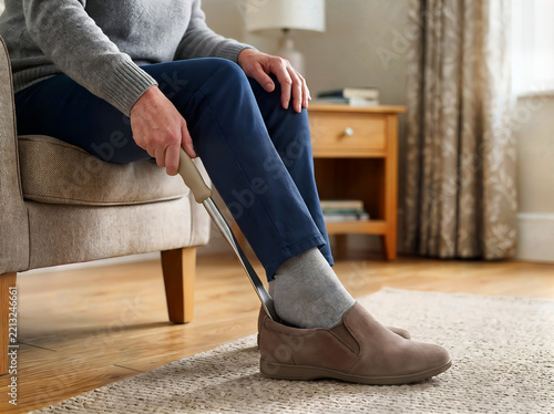 Person using long handled shoehorn to put on comfortable brown shoe