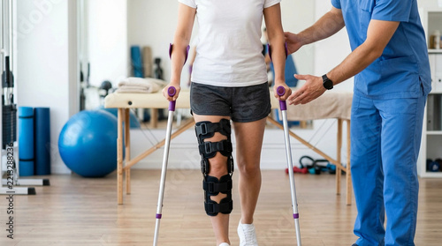Physical therapist assisting patient with knee brace using crutches in rehabilitation center