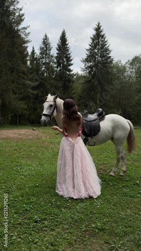 Model in a pink gown holding reins as a white horse turns