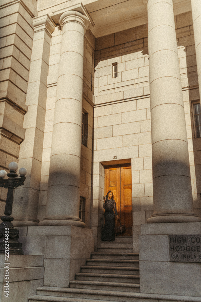 Fototapeta premium Stylish black woman leaving a grand courthouse building in the city