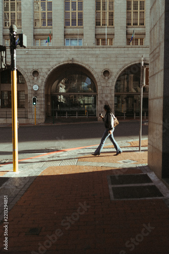 Woman with coffee walks across a sunny city street