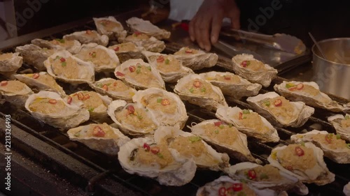Fresh oysters grilled on a metal grill, topped with minced garlic, chopped chili and green onion for a savory dish.