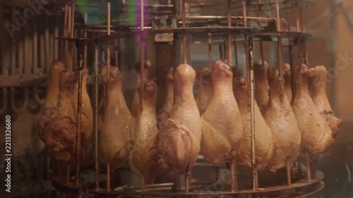 Roasted chicken drumsticks mounted on a rotating vertical grill rack for cooking.