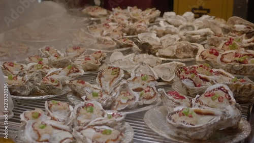 A batch of steamed oysters in half shells, garnished with seasonings, presented as a prepared seafood dish.