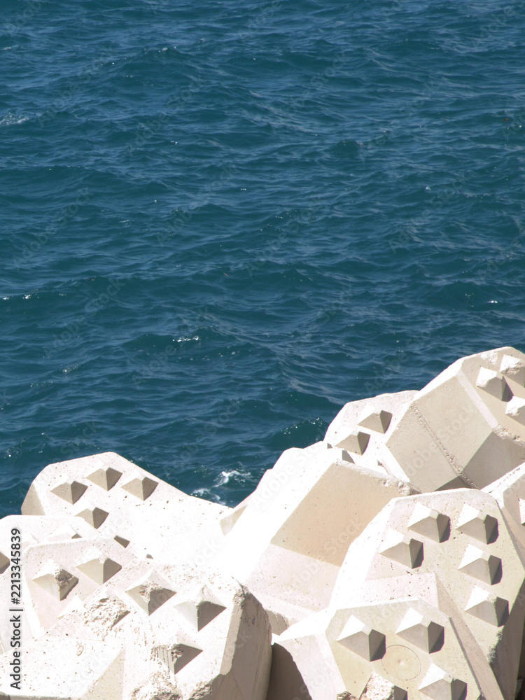 Fototapeta premium Concrete Tetrapod Breakwater Blocks Along Deep Blue Ocean Water