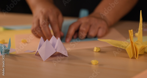 Hands Folding Paper with Origami Crane and Fortune Teller on Table
