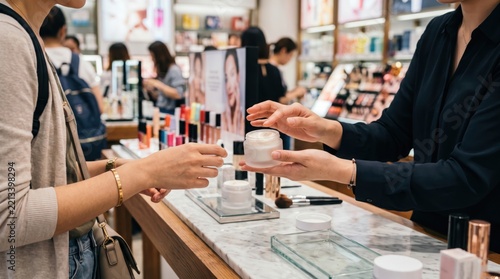 Cosmetic store employee helping tourist choose skin care cream in Myeongdong. Beauty consultant demonstrating product sample to customer in shop. Retail shopping experience and skincare consultation.