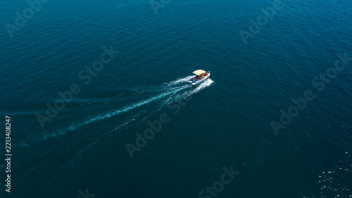 Aerial top-down view of a small motorboat cruising through deep blue waters, leaving a white foamy wake behind as it glides across the serene open surface.