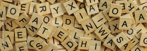 Pile of wooden tiles with various letters in big amount scattered on white board, closeup view