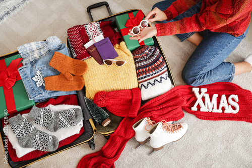 Female traveler packing sunglasses into suitcase at home on Christmas eve, to...
