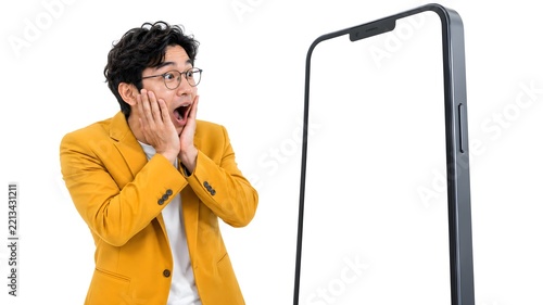 Shocked young man in yellow blazer with hands on cheeks staring at giant smartphone on white background, copy space