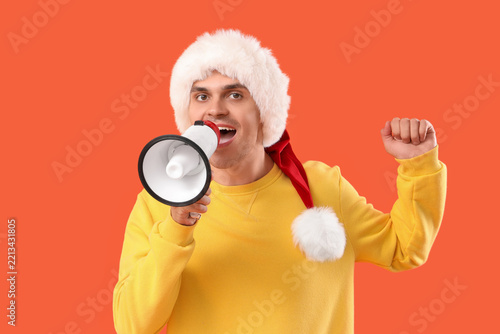 Happy young man in Santa hat with megaphone on orange background