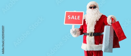 Cool Santa Claus holding board with word SALE and shopping bags on blue backg...