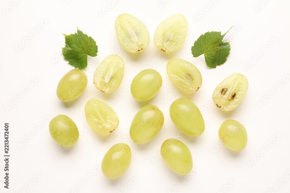 Fototapeta premium Fresh ripe grapes and green leaves on white background, flat lay