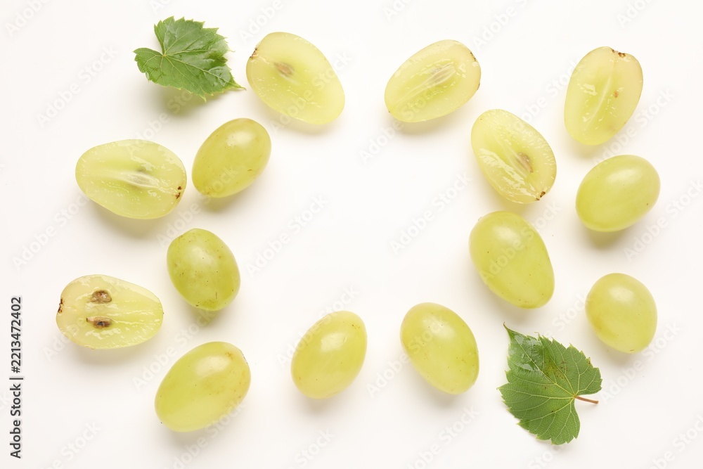 Fototapeta premium Fresh ripe grapes and green leaves on white background, flat lay. Space for text