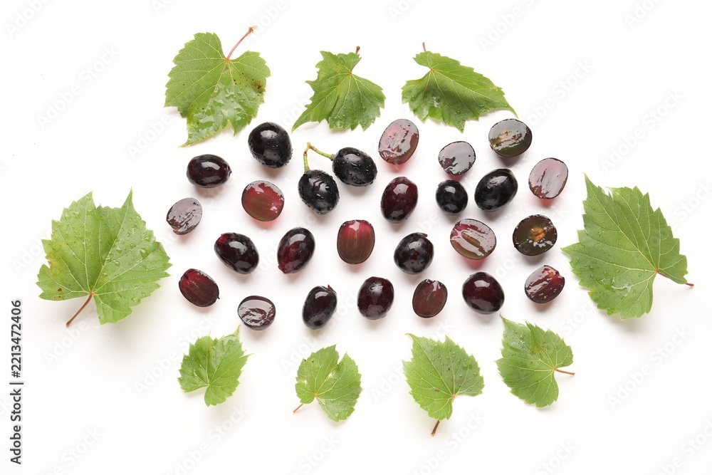 Fototapeta premium Fresh ripe grapes and green leaves on white background, flat lay