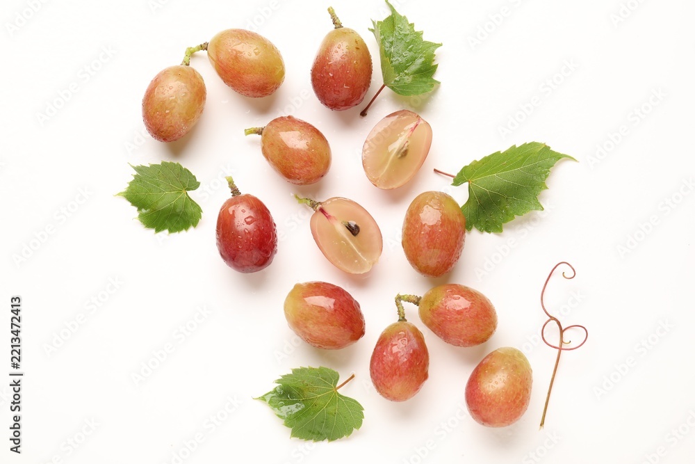 Fototapeta premium Fresh ripe grapes and green leaves on white background, flat lay