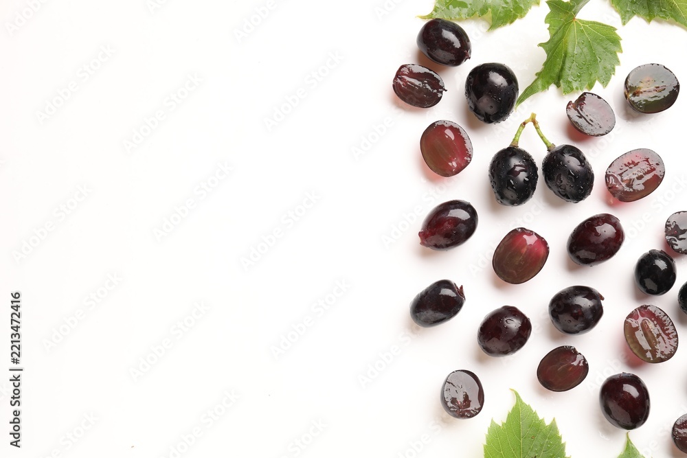 Naklejka premium Fresh ripe grapes and green leaves on white background, flat lay. Space for text