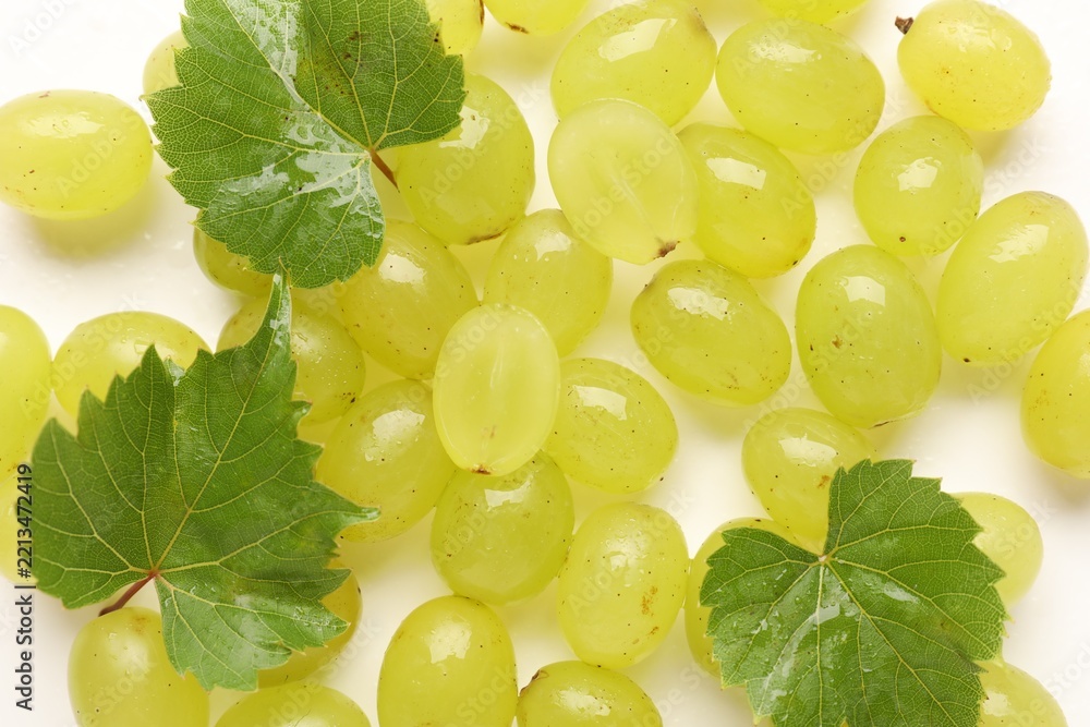 Fototapeta premium Fresh ripe grapes and green leaves on white background, top view