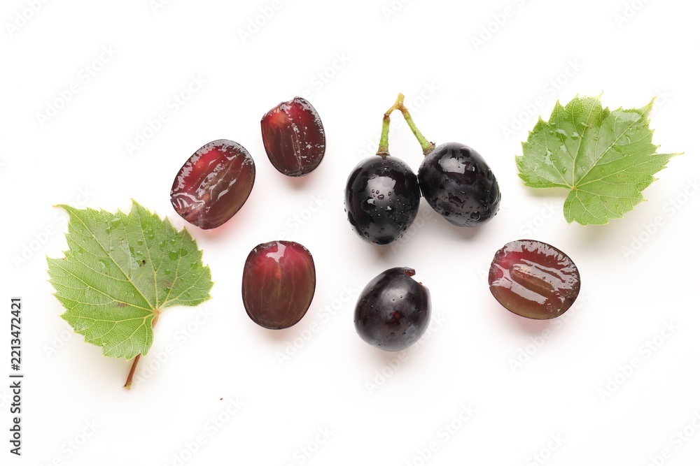Fototapeta premium Fresh ripe grapes and green leaves on white background, flat lay