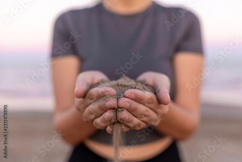 Woman holding sand in cupped hands with sand falling through fingers on beach