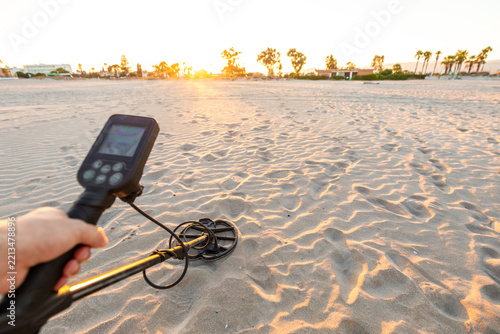 Hand holding metal detector on sandy beach at sunset first person view